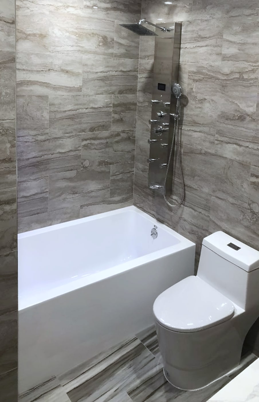 Bathroom with stone-look tile, white tub, toilet and shower panel