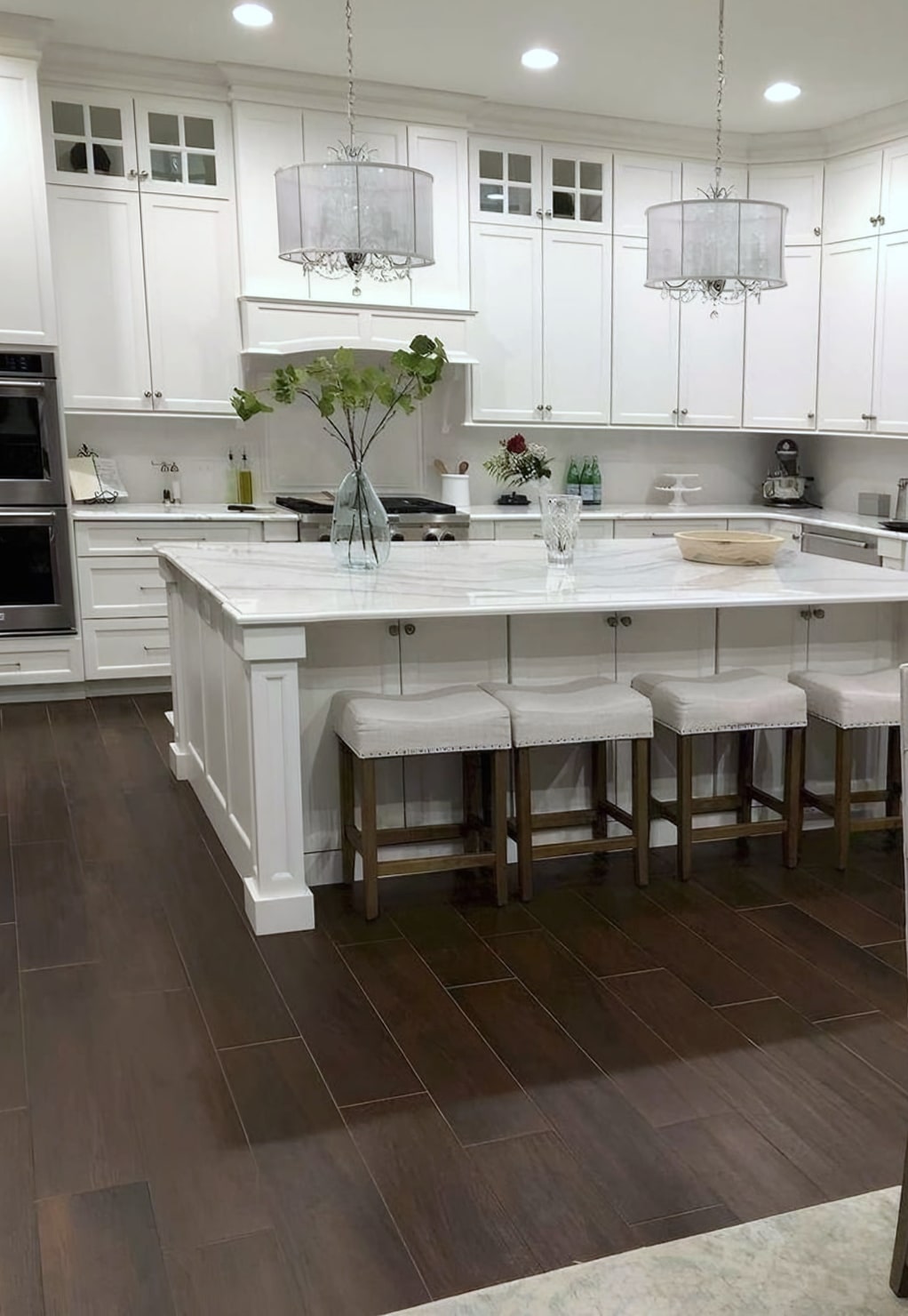 White kitchen with island, bar stools, double oven and dark plank floor