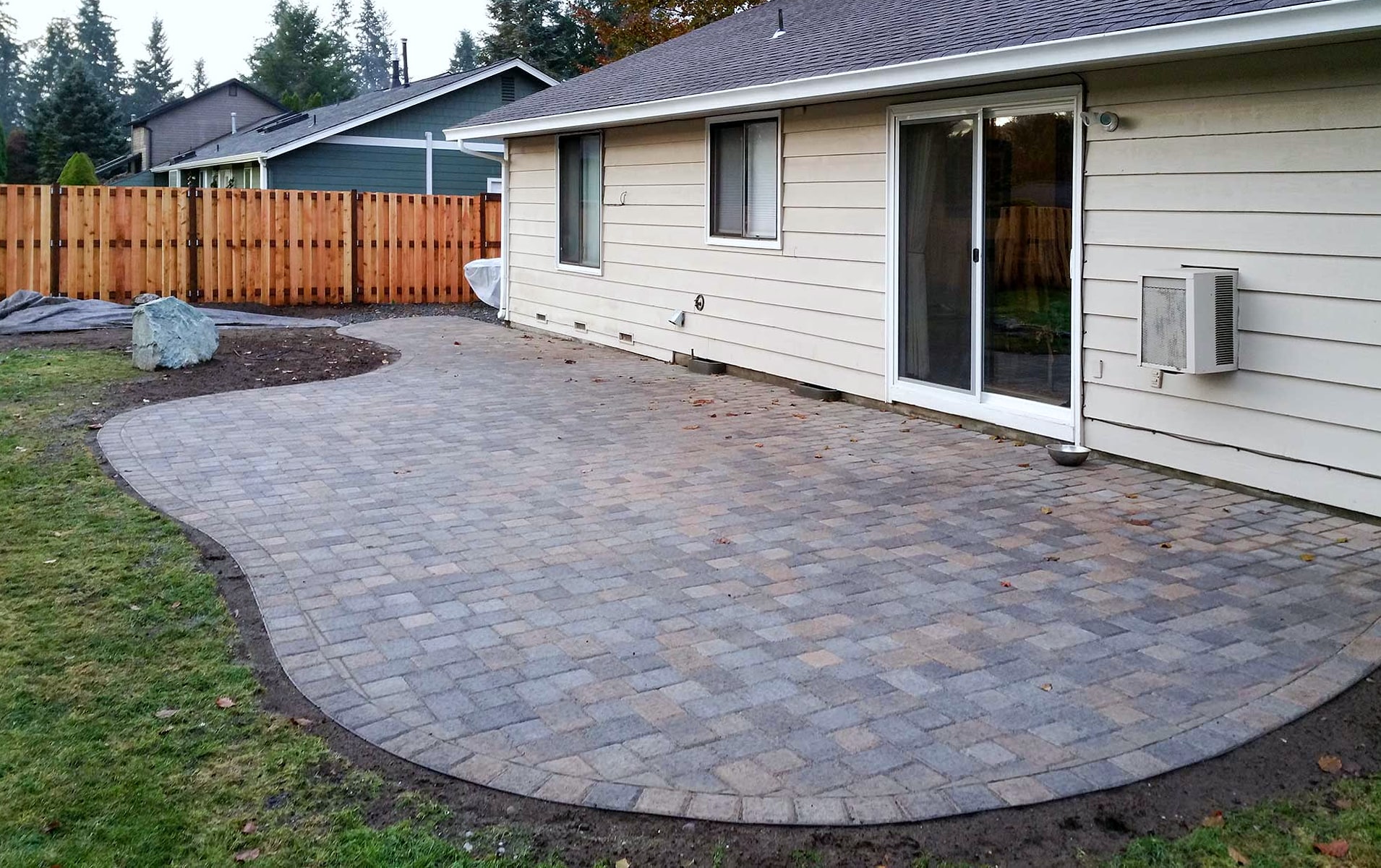 Curved paver patio behind a house with wooden fence