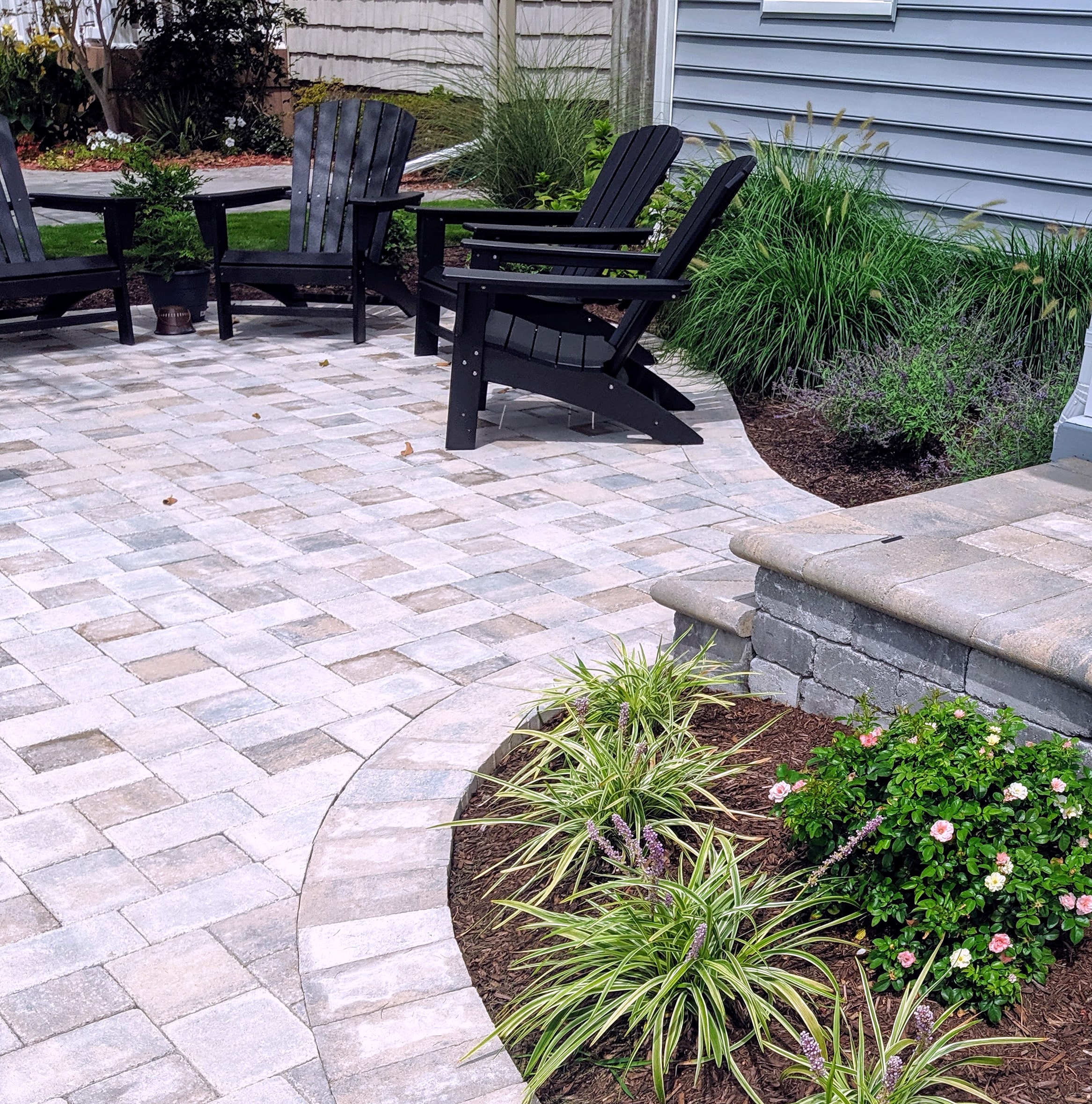 Paver patio with curved border, retaining seat wall, black chairs and plantings